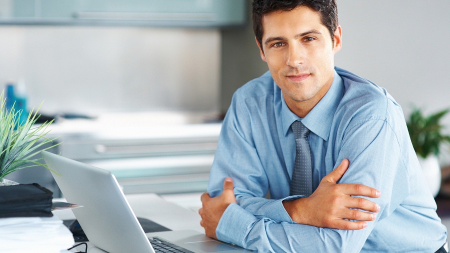 Happy executive sitting in front of laptop with arms folded